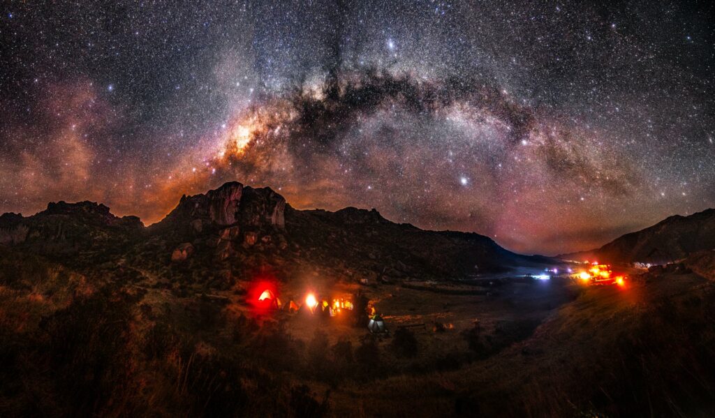 Vía Láctea sobre las montañas de Marcahuasi, en los Andes de Lima, Perú, con fogatas de un campamento al pie